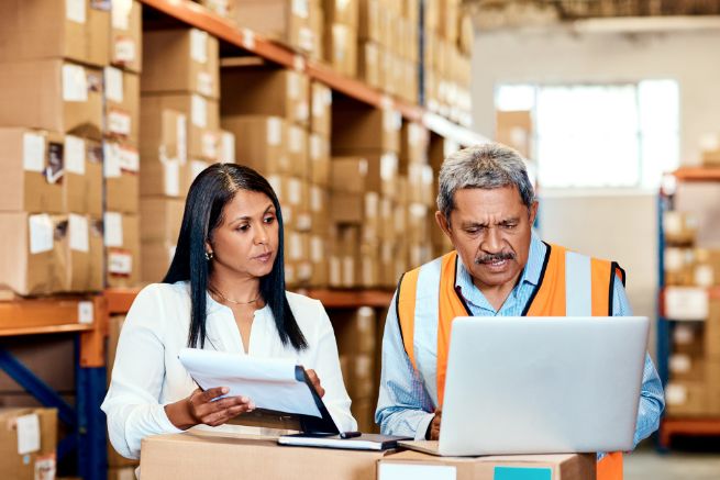 Shot of a mature man and woman going through paperwork while using a laptop in a warehouse. Consignment Agreement.